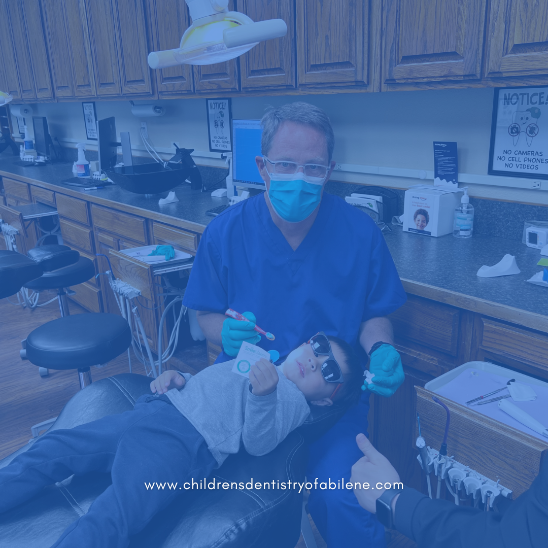 Pediatric dentist in blue scrubs and mask treating young patient in modern dental office