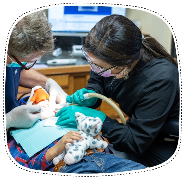Pediatric dentist examines young patient's teeth in dental office treatment room.