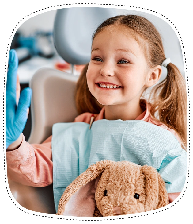 Happy young girl holding teddy bear in dental office waiting room.
