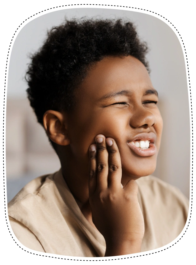 Young boy touching his cheek, smiling brightly in a neutral dental office setting.