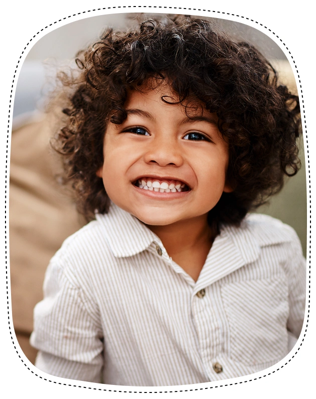 Smiling young child with curly dark hair wearing light striped shirt indoors