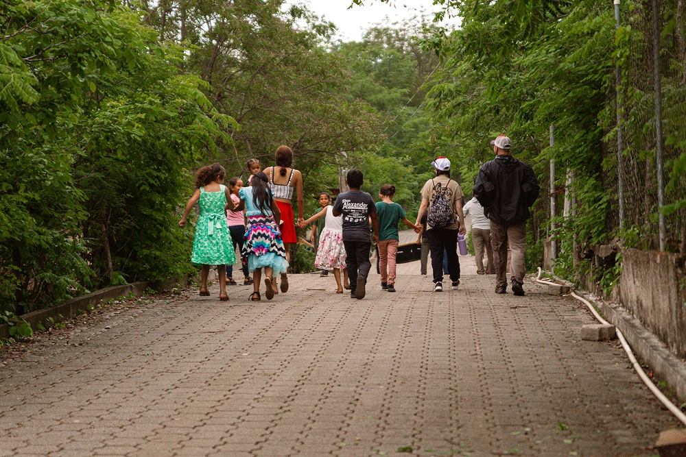 Group of children and adults walking together on a tree-lined brick pathway outdoors.