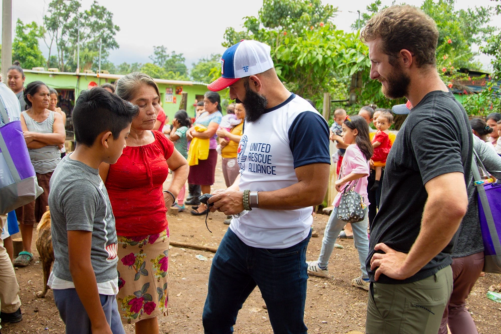Community volunteer in white cap distributes items to children outdoors at a dental outreach event.