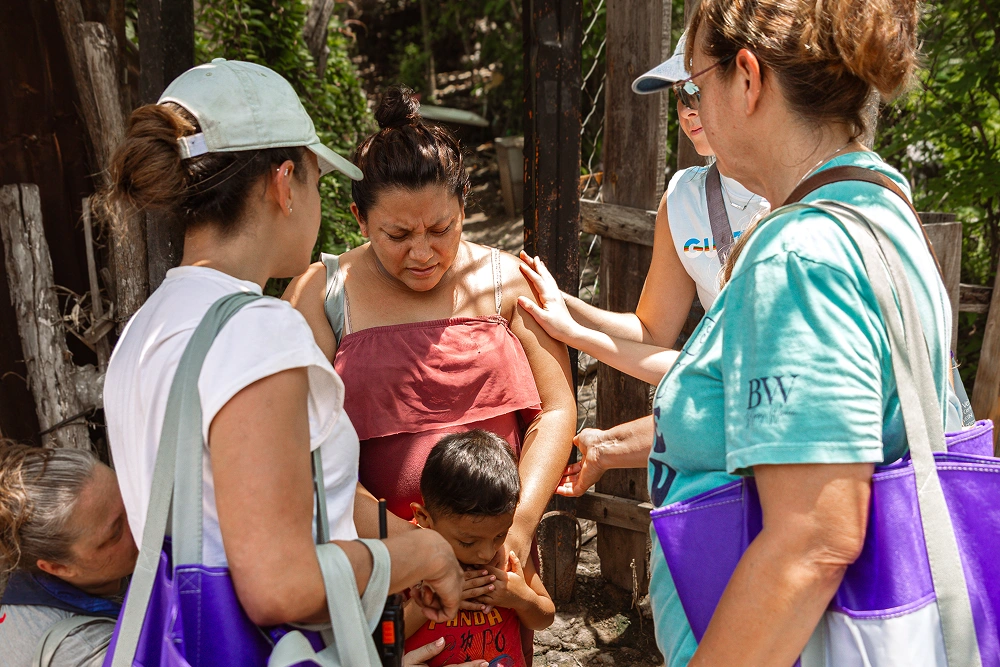 Three healthcare workers examine a young child's teeth outdoors in a community setting.