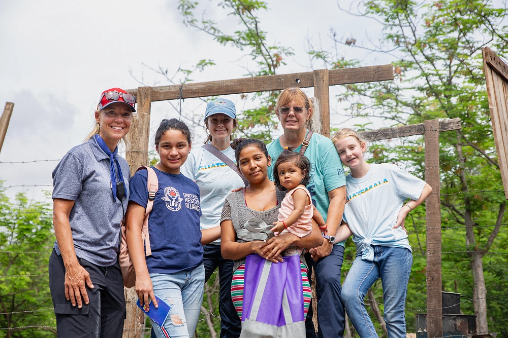 Group of dental professionals and children posing together in front of wooden structure outdoors.