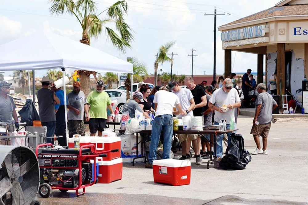 Community outdoor event with vendors and attendees gathered in parking lot on sunny day.