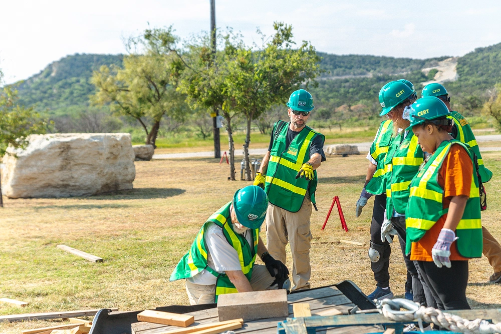 Construction workers in safety vests working outdoors on a sunny day in a grassy area.