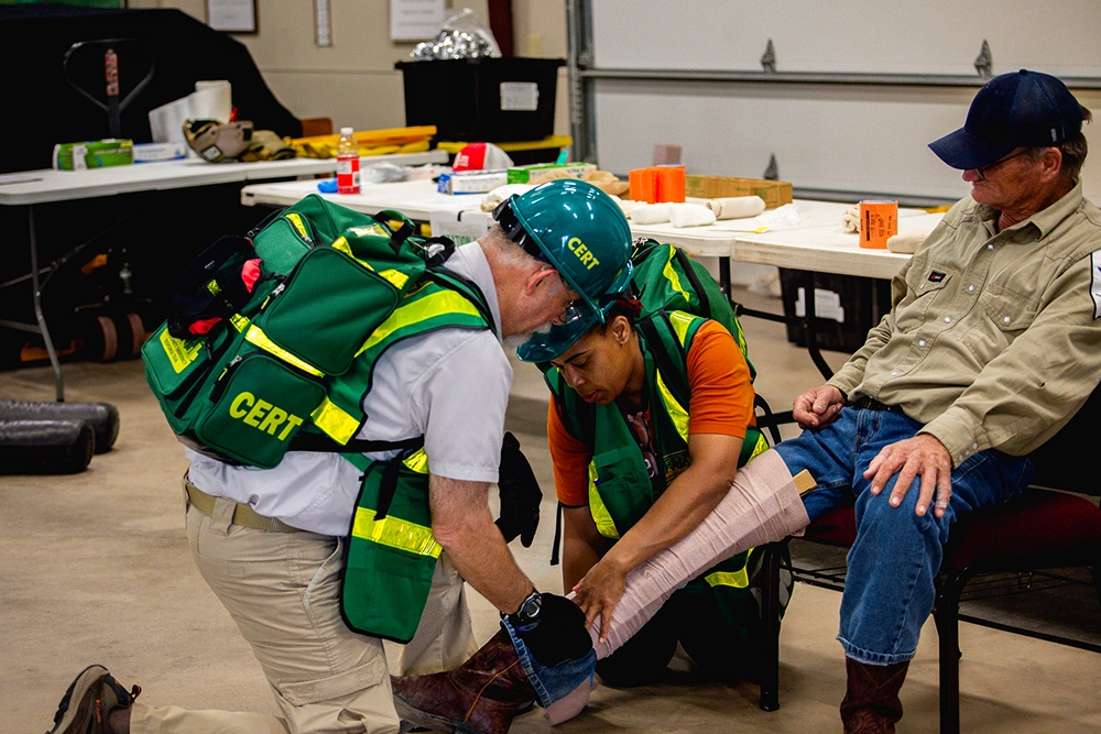 Children in green safety vests practicing first aid or medical training with instructor outdoors.