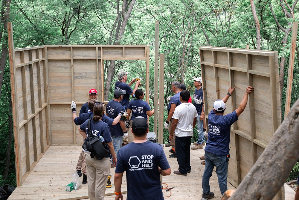 Group of children in blue shirts exploring wooden structure outdoors among trees.