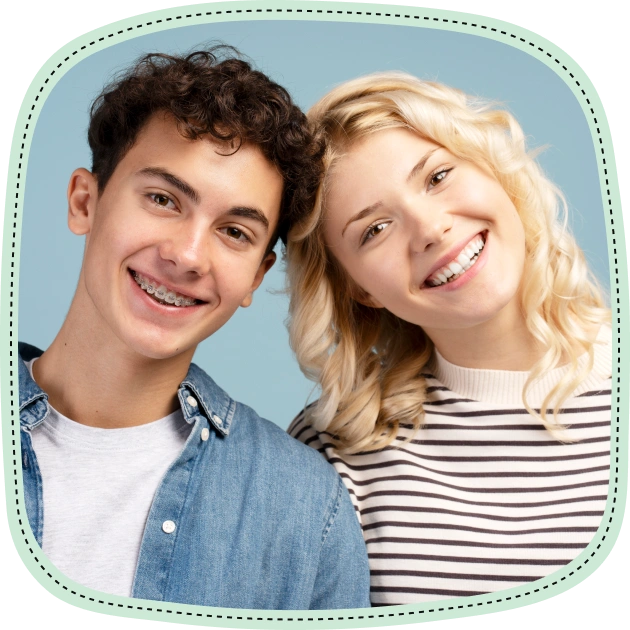 Two smiling teens pose together against blue background for children's dentistry practice portrait.