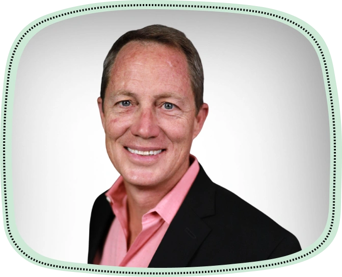 Professional headshot of male dentist smiling in pink shirt and black jacket against white background.