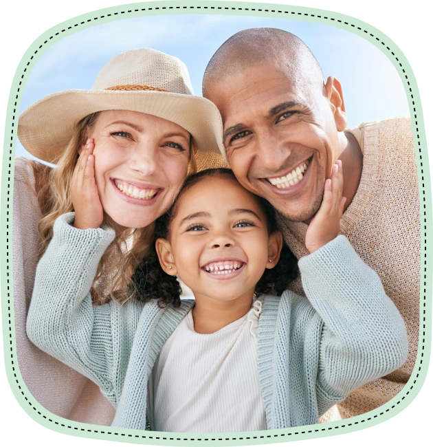 Happy family of three smiling outdoors in warm, sunny setting.