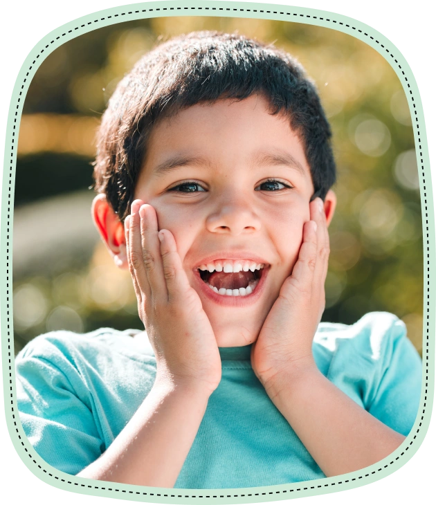 Happy young boy in turquoise shirt smiling brightly outdoors.