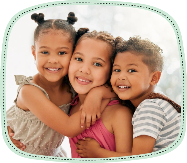 Three smiling children hugging together in a studio portrait setting.