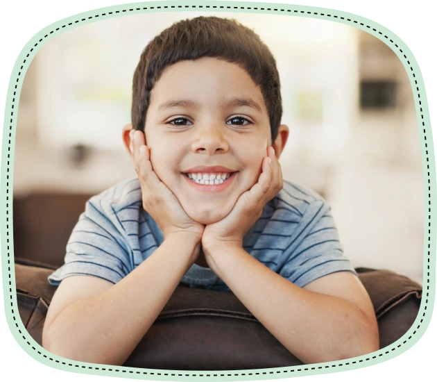Smiling young boy with hands on face, wearing blue striped shirt indoors.