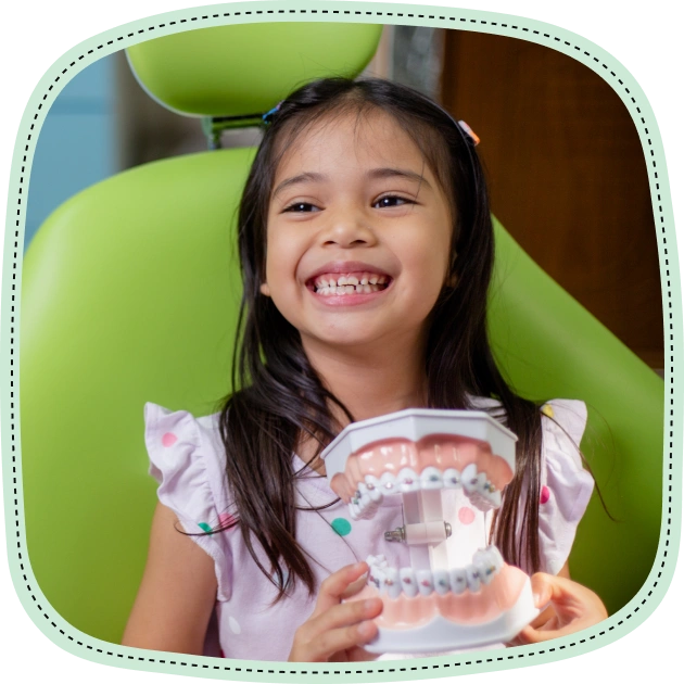 Young girl smiling brightly while holding a large dental model showing teeth and gums.