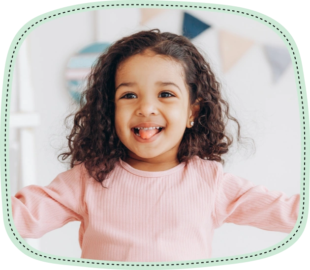 Smiling young child with curly dark hair wearing pink shirt in bright dental office setting.