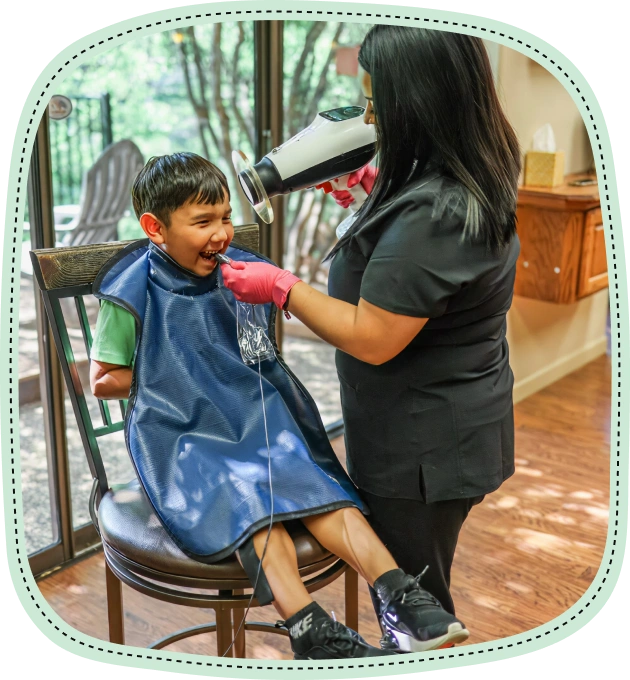 Pediatric dentist examining young boy's teeth in dental office chair.