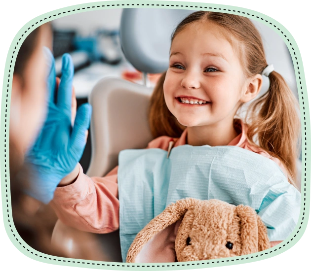 Young girl smiling in dental chair with dentist holding mirror during checkup.