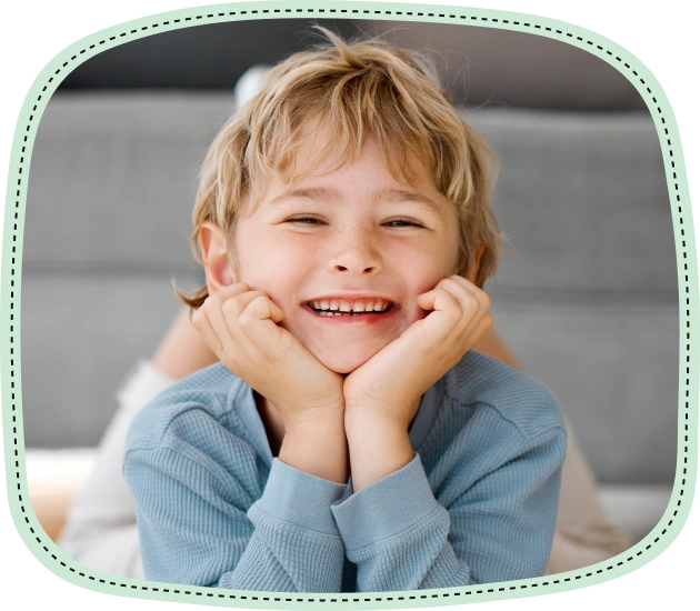 Happy young boy smiling brightly while resting chin on hands indoors.