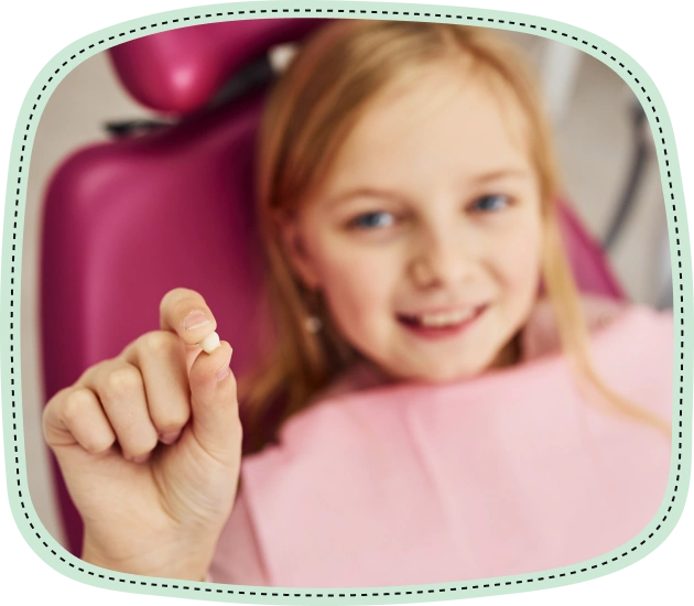 Young girl in pink shirt smiling, pointing at tooth in dental office setting.