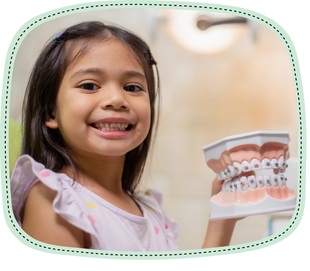 Young girl smiling at dental office with teeth model visible in background.