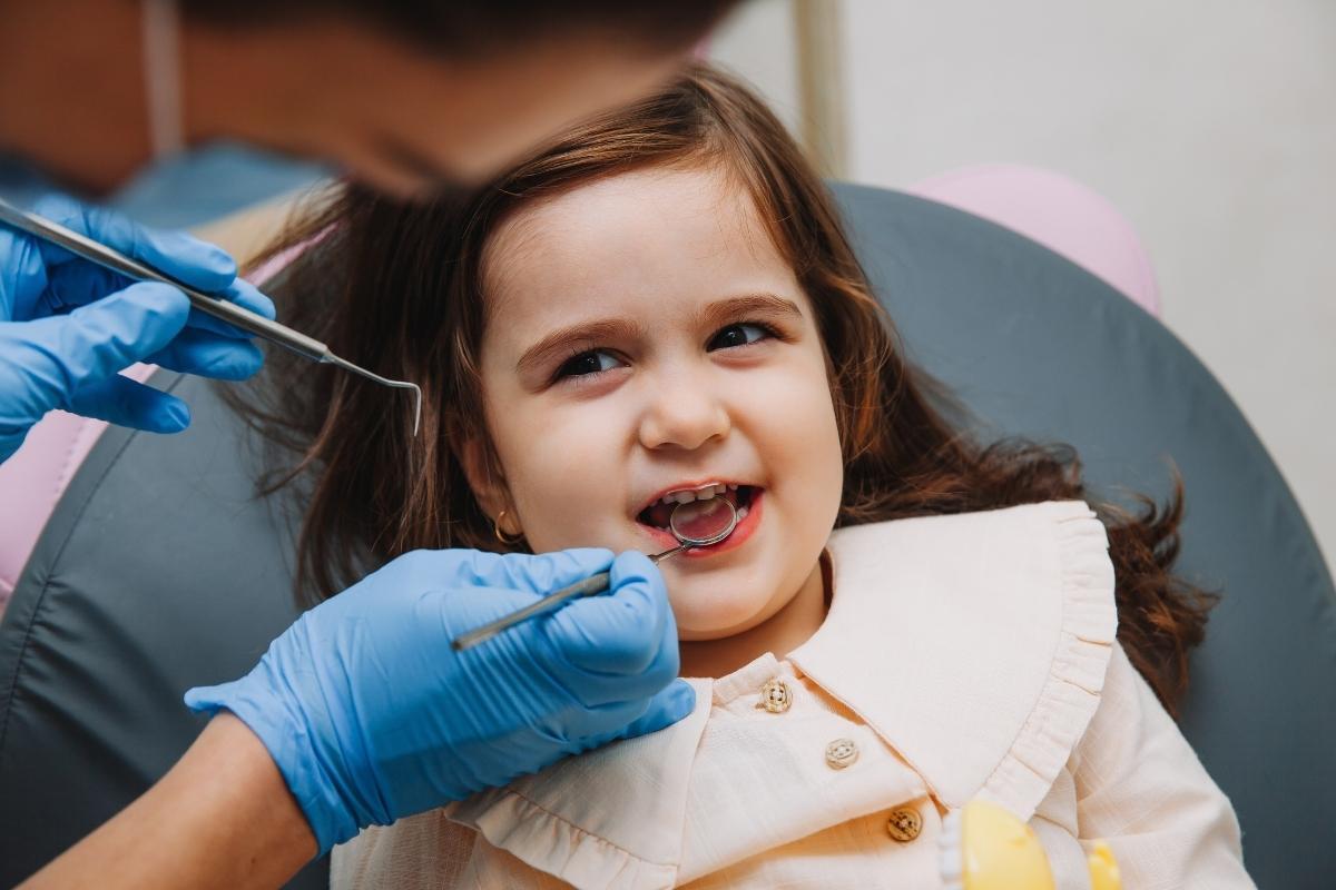Young girl smiling in dental chair during examination by dentist in blue gloves.