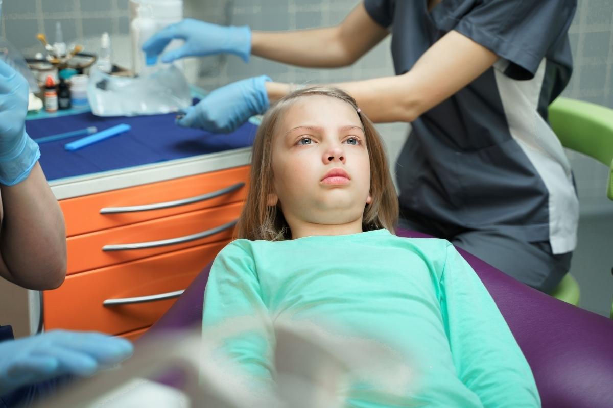 Child patient in dental chair during examination with dentist wearing gloves.